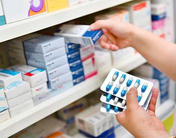 Pharmacist holding medicine box and capsule pack in pharmacy drugstore.